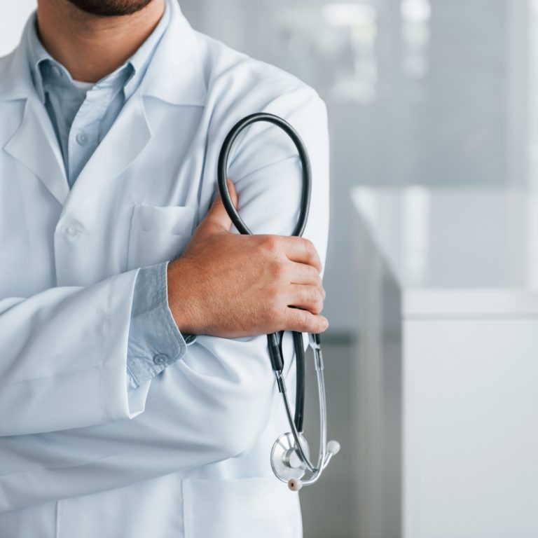 Stethoscope in hands. Professional medic in white coat is in the clinic